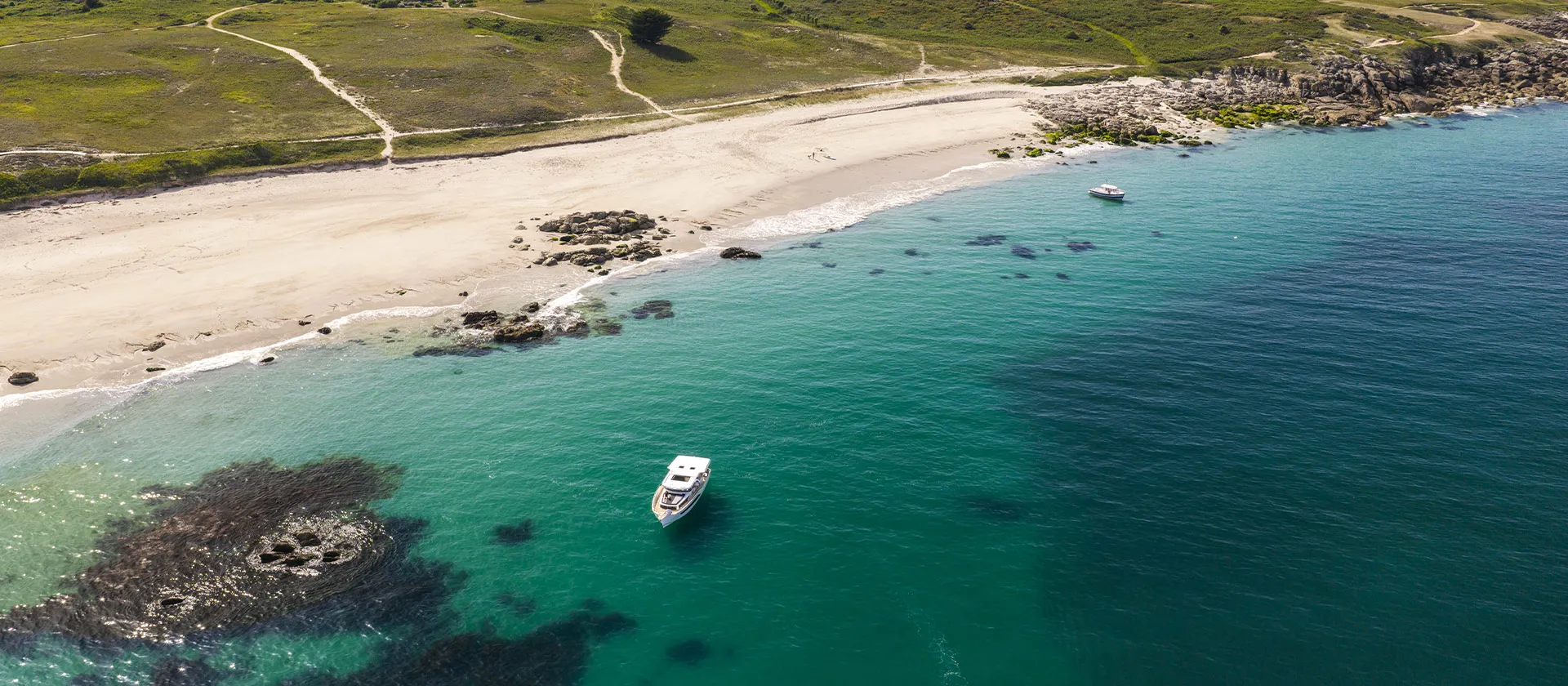A Delphia at anchor in a clear bay off a sandy beach
